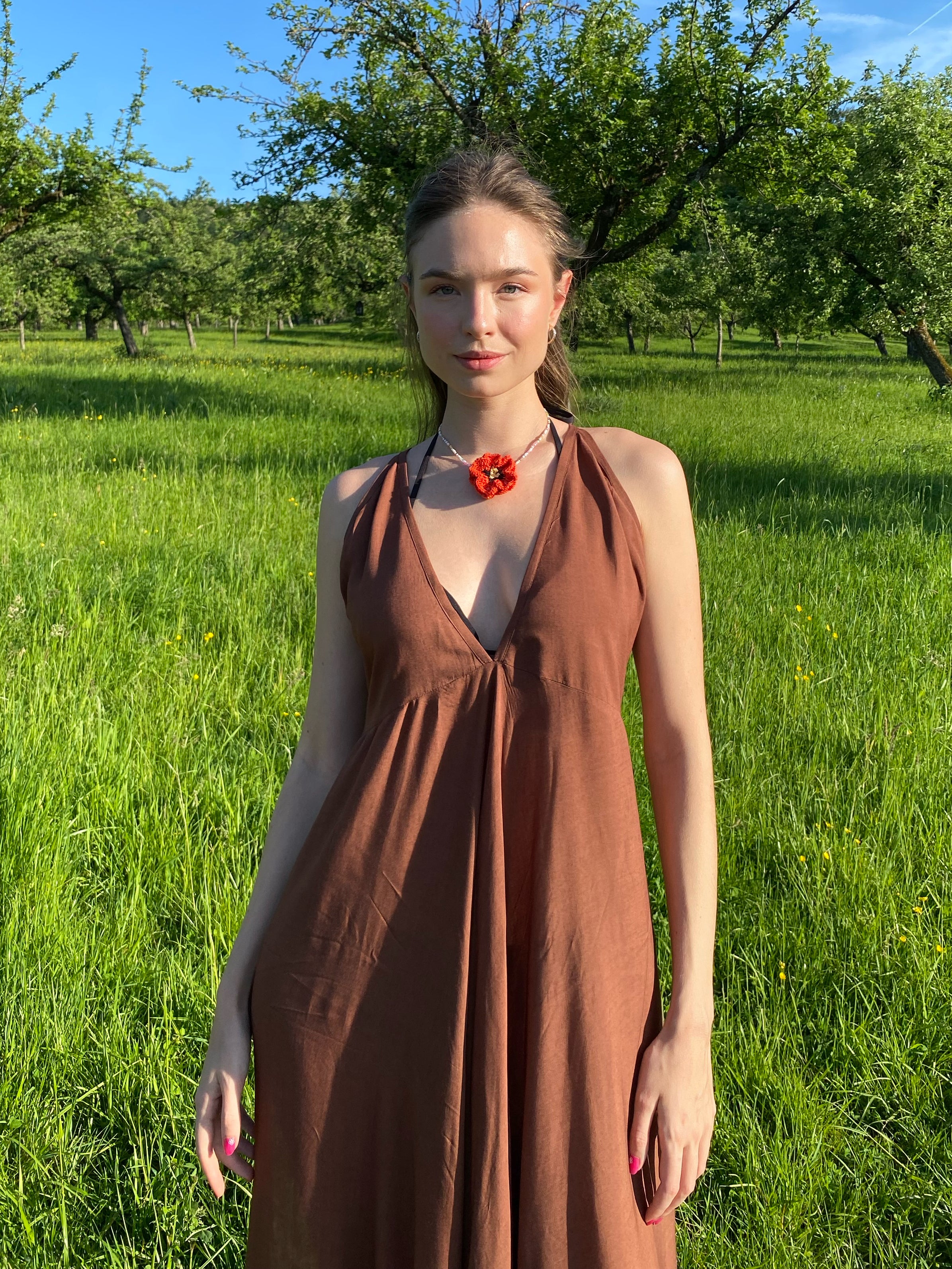 Woman wearing a flowy, hand-dyed brown halter maxi dress with open back and high slit, styled as boho stye resort wear under in the field.