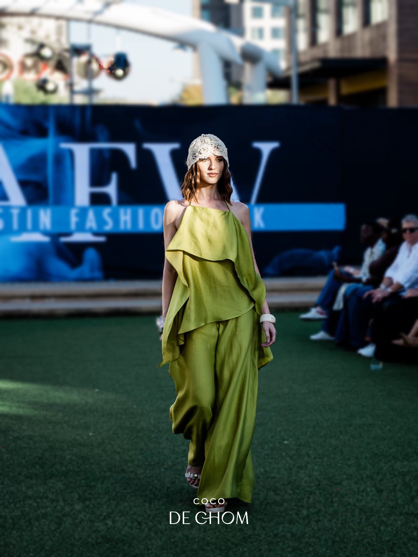 Model wearing a green lime resort wear beach cover up outfit with a headpiece at a fashion event, with 'Austin Fashion Week' branding in the background.