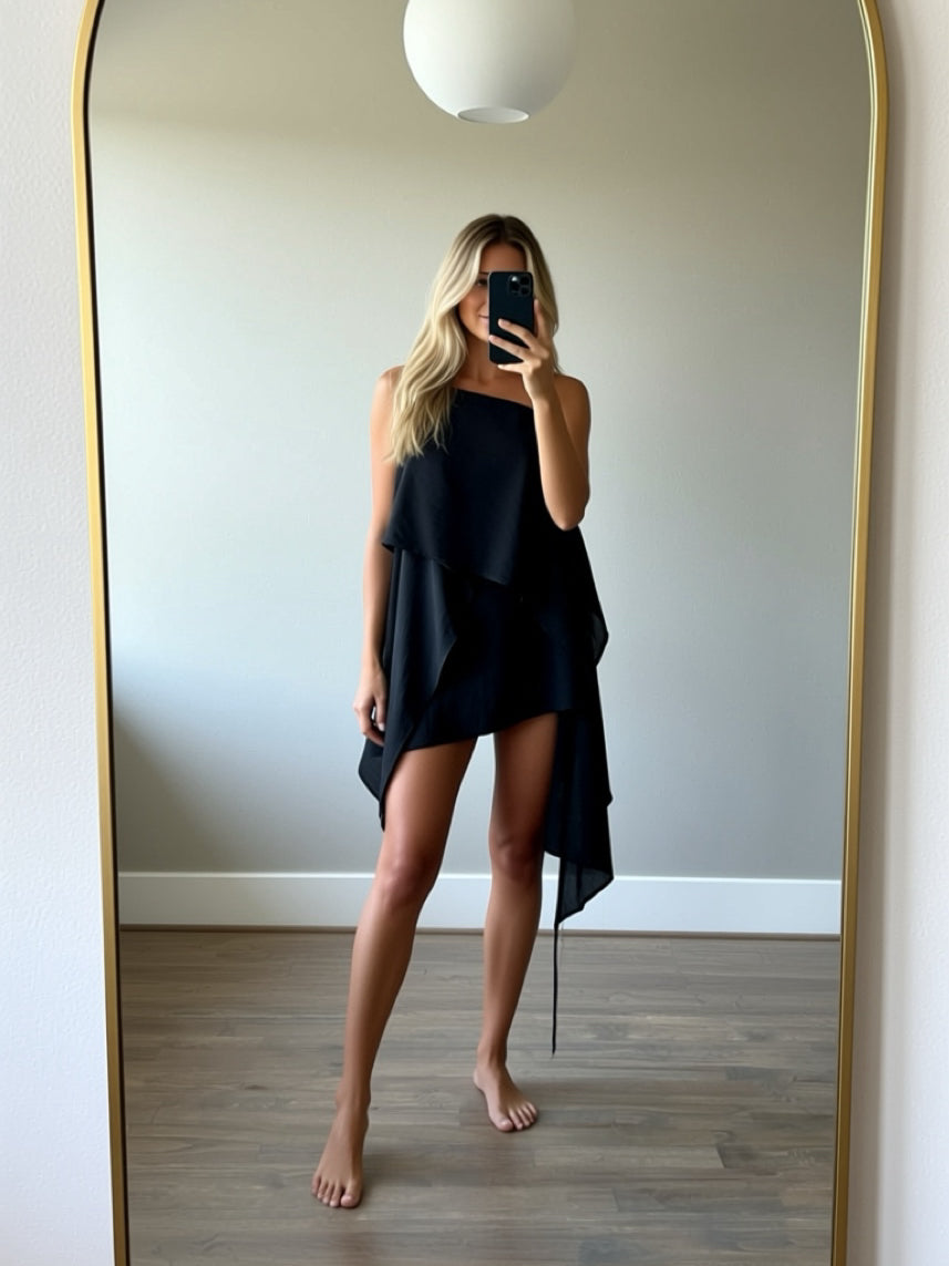 Woman in a black flowy kaftan top standing on a balcony with a scenic view of trees and water.