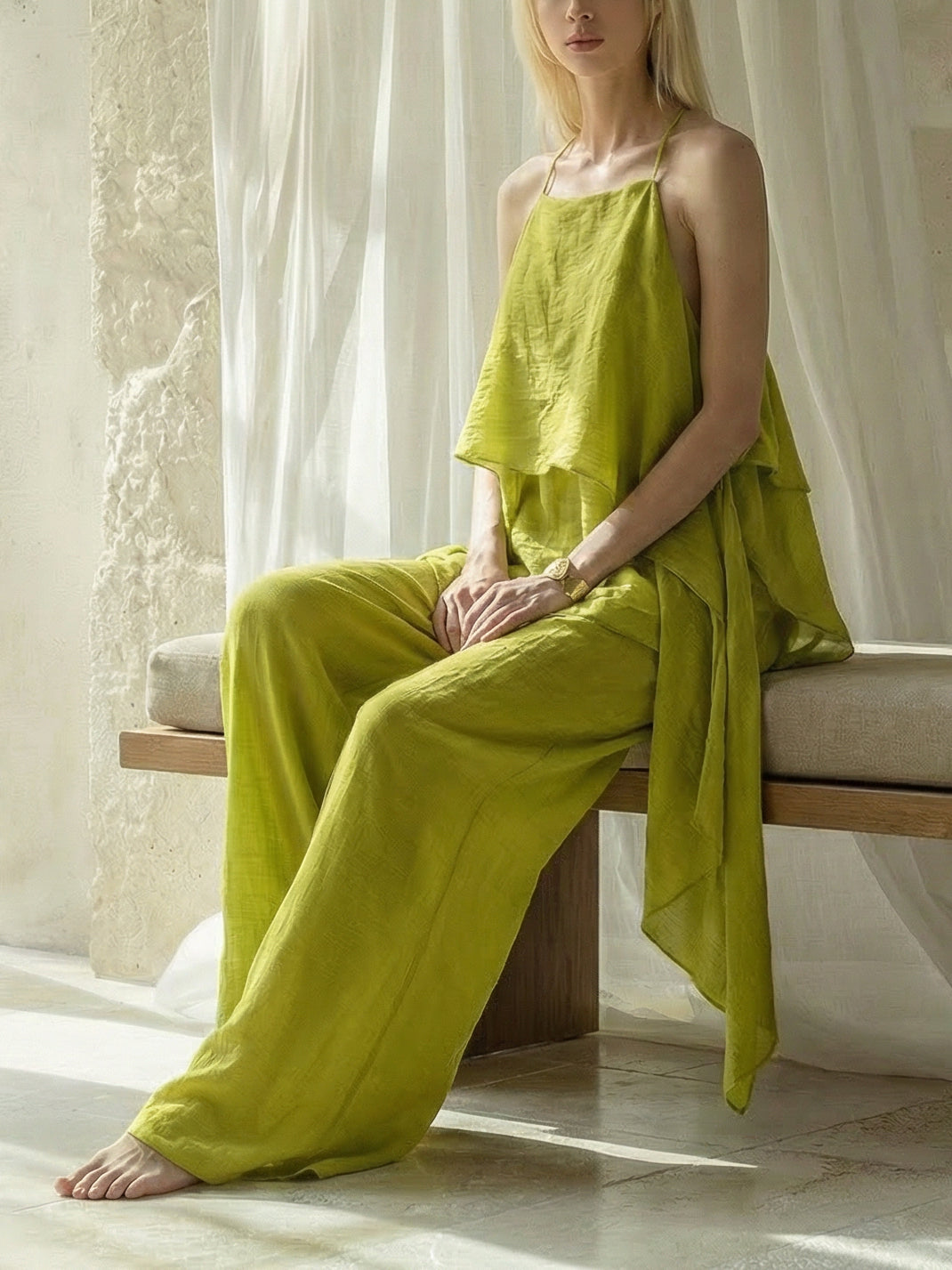 Woman in a lime beach cover up top with wide leg pants , look resort outfit with a wide-brimmed hat standing in front of a stone archway.