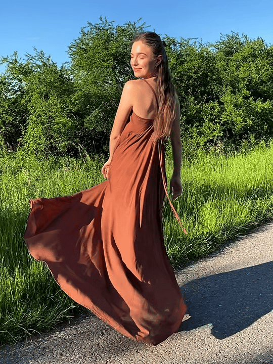Woman wearing a flowy, hand-dyed brown halter maxi dress with open back and high slit, styled as boho stye resort wear under in the field.