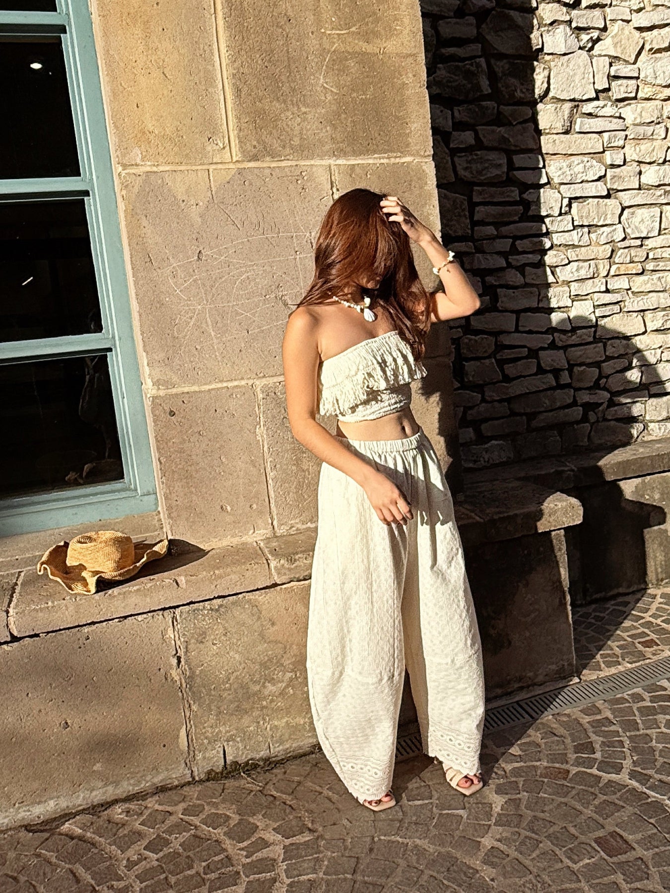 Woman wearing ivory wide leg cotton pants with lace hem, styled barefoot with straw tote — boho beach outfit for summer, handmade resortwear