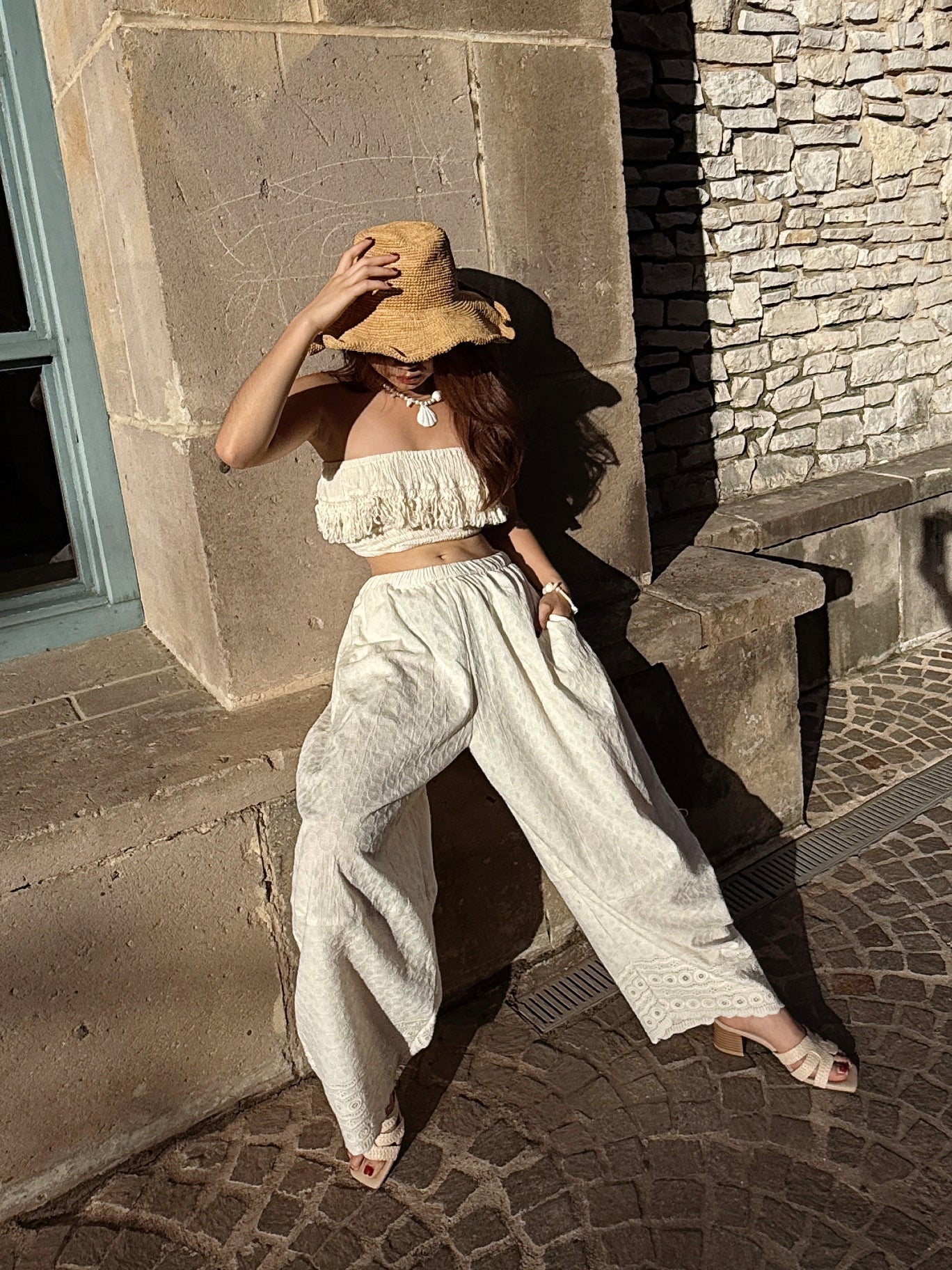 Woman in a white outfit and straw hat sitting on stone steps.