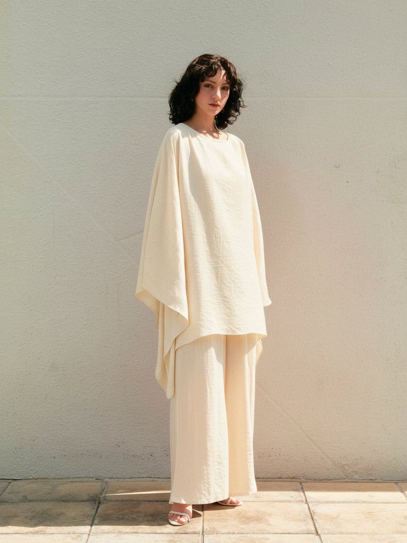 Woman wearing a white mini kaftan top beach cover up tunic, one size fits most, long sleeves with high-low hem, lightweight resort vacation wear, standing against a white wall in bobo style.