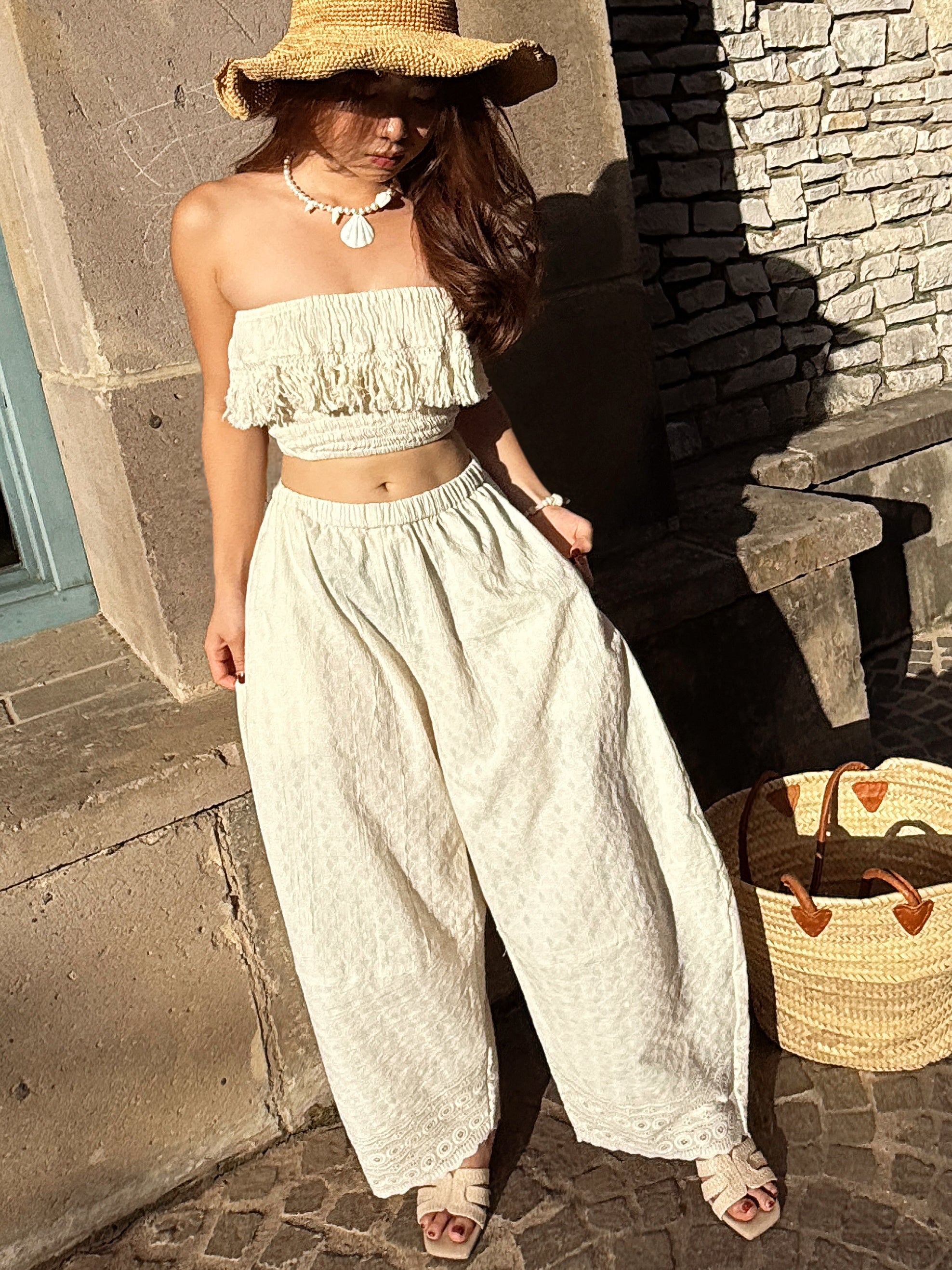 Model wearing white cotton lace fringe tube top with boho pants, posing outdoors in natural sunlight – handmade resortwear outfit