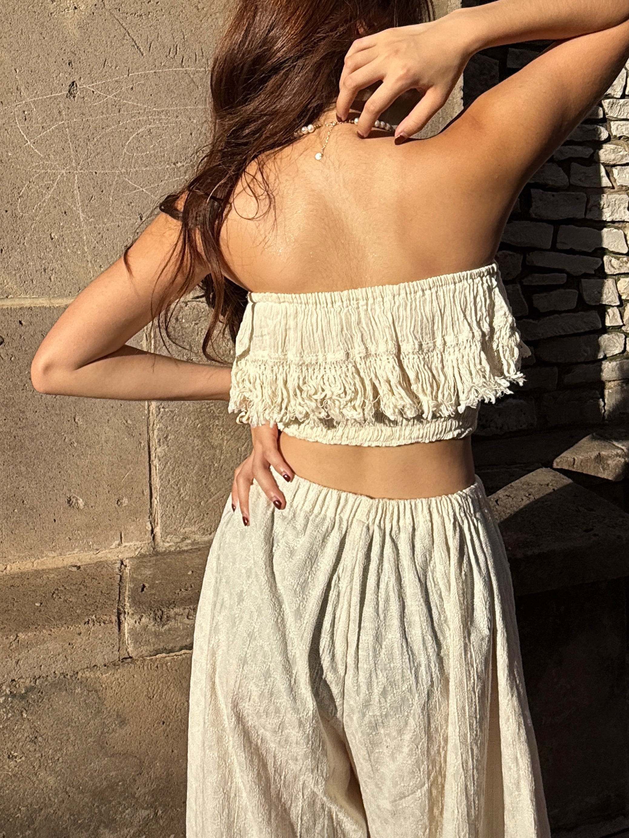 Model wearing white cotton lace fringe tube top with boho pants, posing outdoors in natural sunlight – handmade resortwear outfit