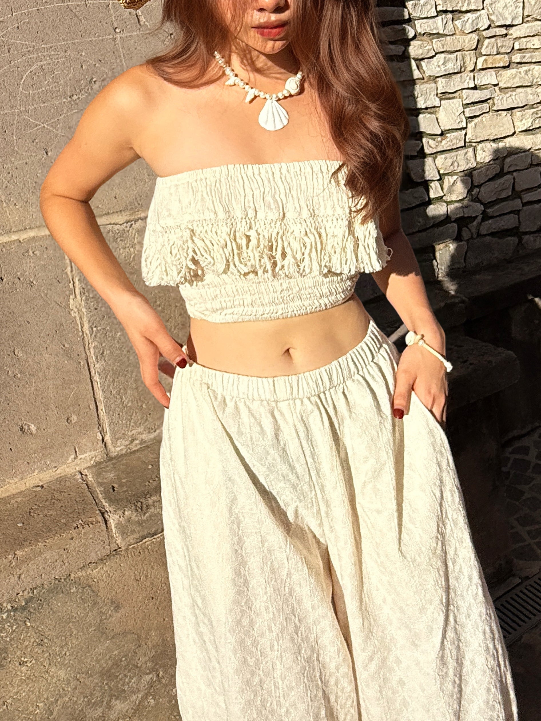 Model wearing white cotton lace fringe tube top with boho pants, posing outdoors in natural sunlight – handmade resortwear outfit