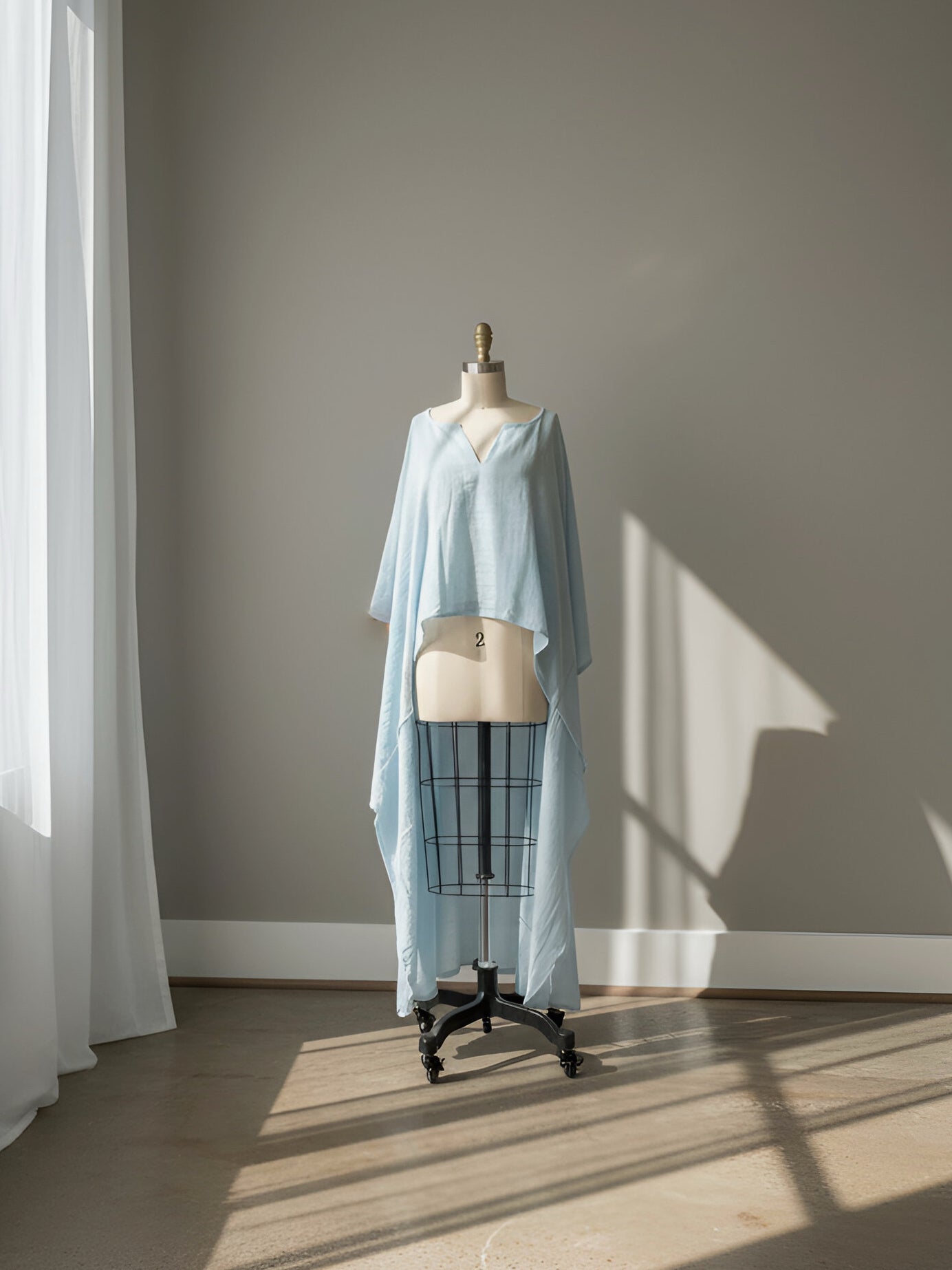 Mannequin wearing a light blue cotton linen kaftan top light blue worn as beach coverup relaxed fit  in a room with sunlight casting shadows on the wall.
