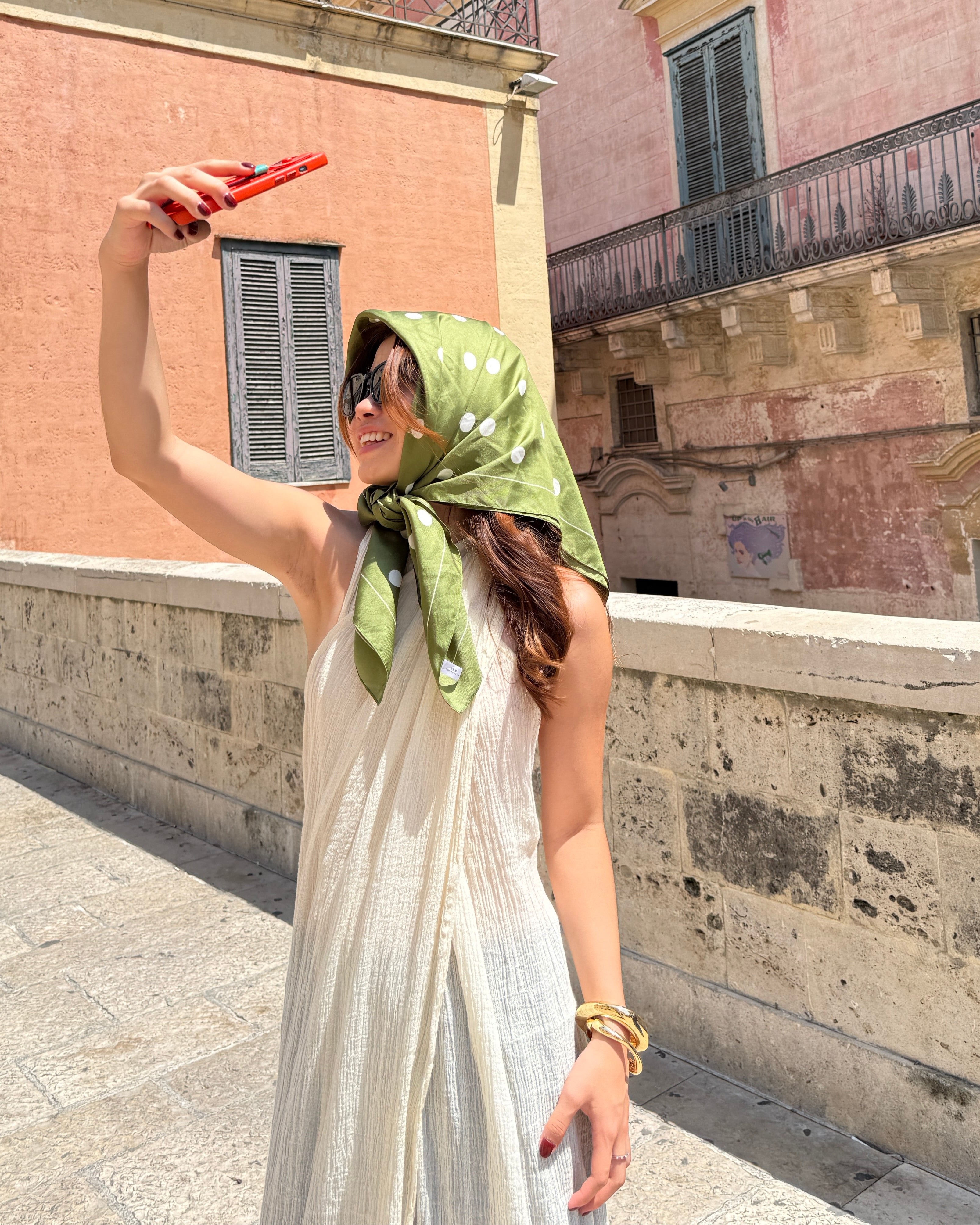 Woman taking a selfie with a green headscarf and white cotton maxi dress in front of a building
