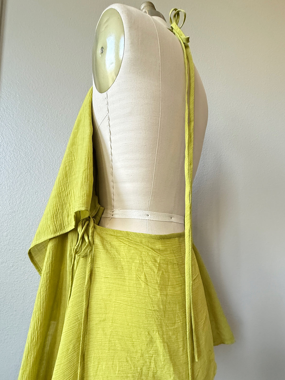 A lime green textured wrap or shawl draped over a cream-colored dress form mannequin, shown against a plain off-white wall.