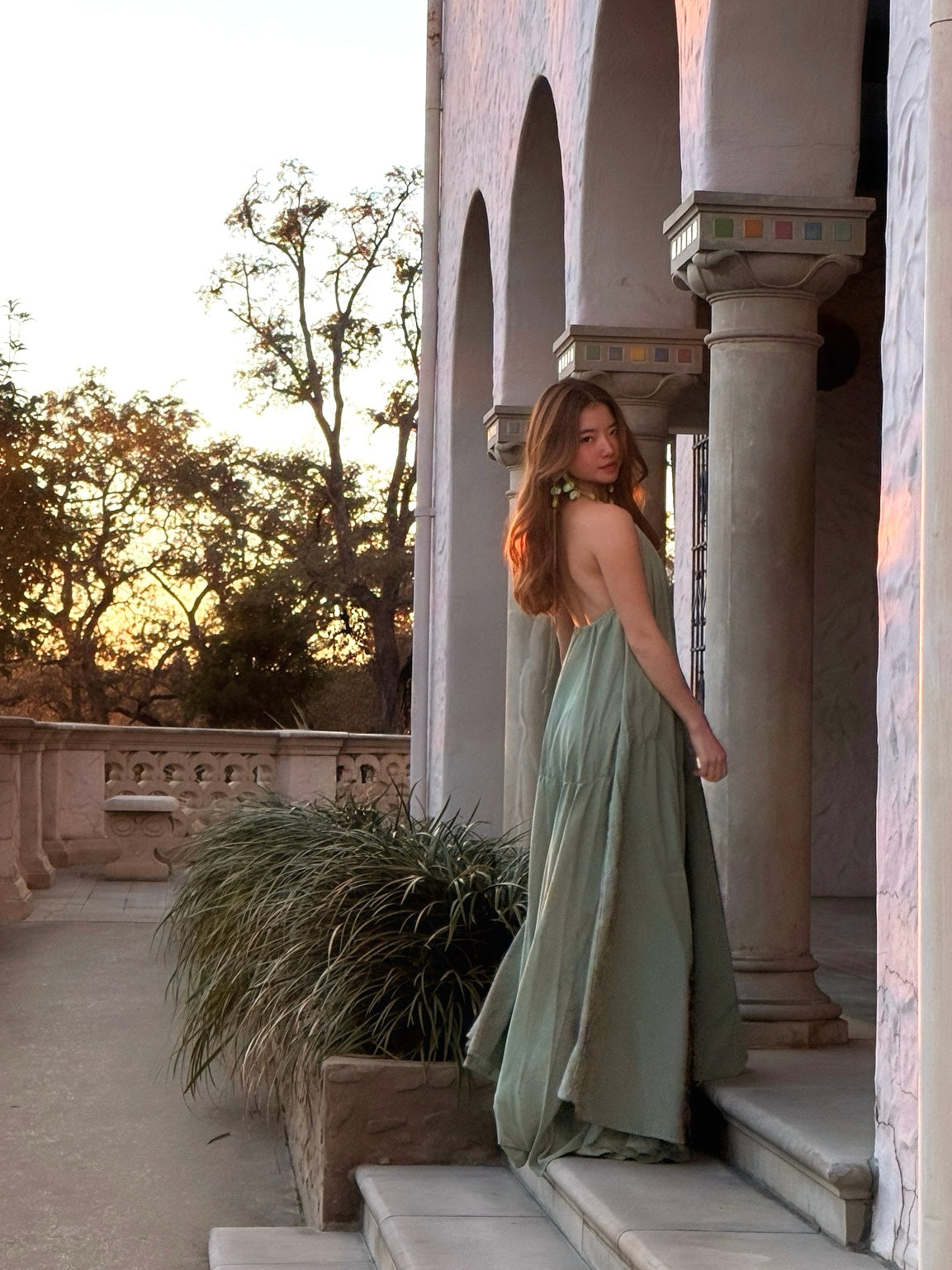 Woman in a green open back dress standing on steps with a scenic background
