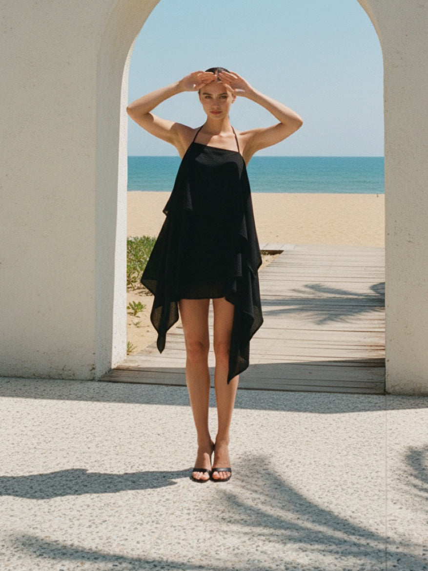 Woman in a black layer top beach coverup dress standing in front of an archway with a beach view.