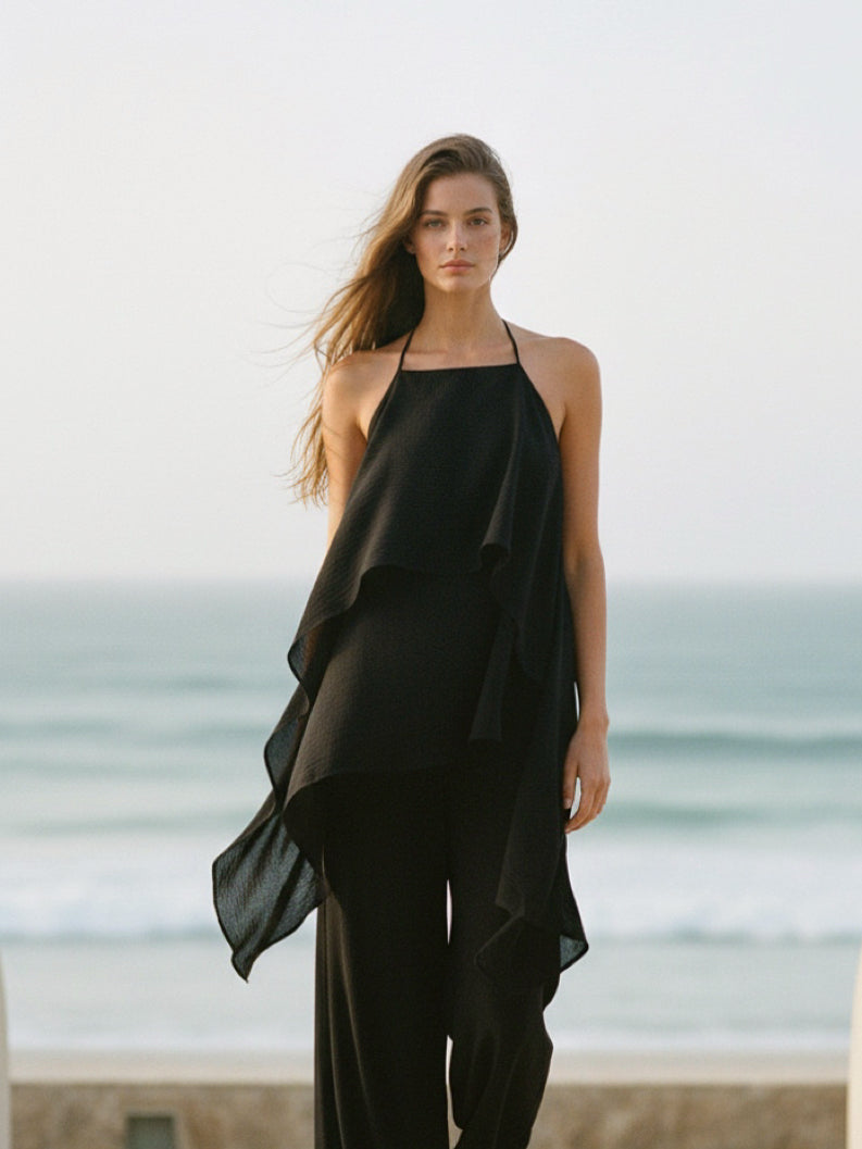 Woman wearing a black halter top and pants on a beach, black beach cover up top