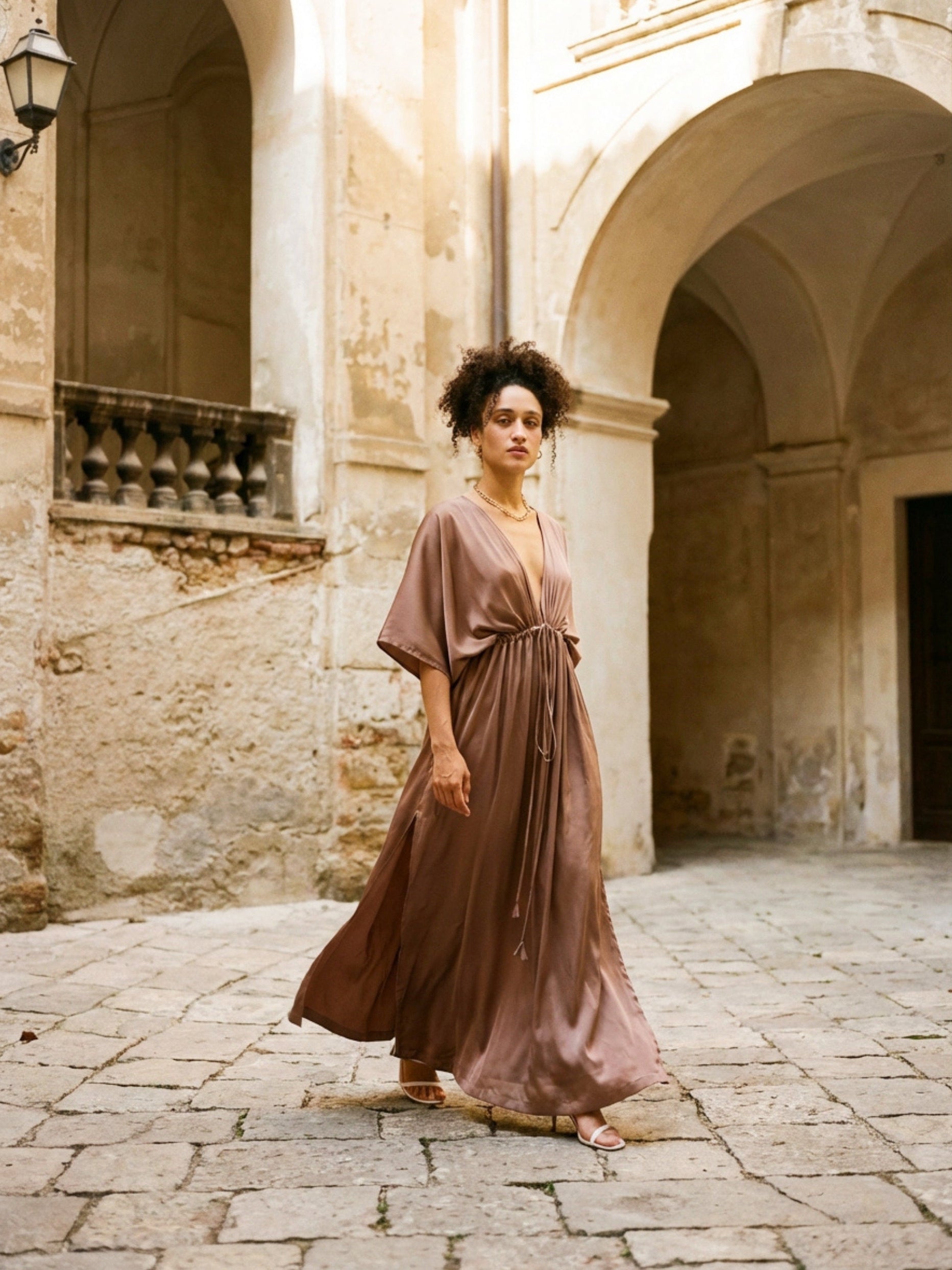 Woman wearing a long mocha kaftan maxi dress with deep V-neck and self-tie waist, styled as resort wear and a beach wedding guest dress by COCO DE CHOM