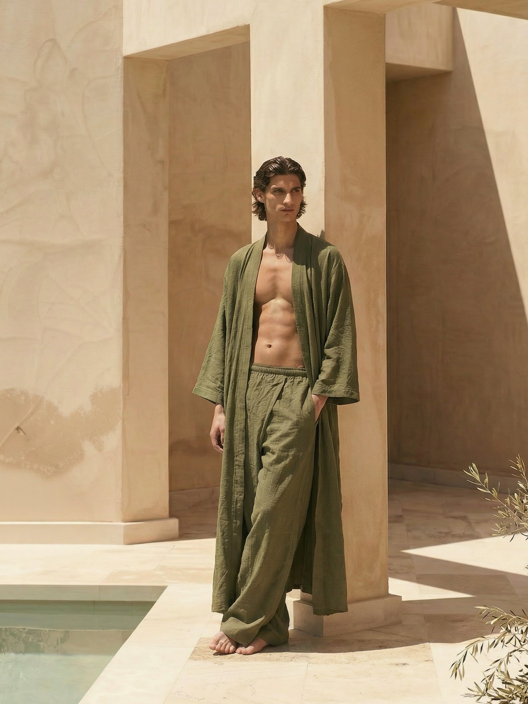 Man wearing a green olive long robe standing in a sunlit room with oversized pants resort set during vacation