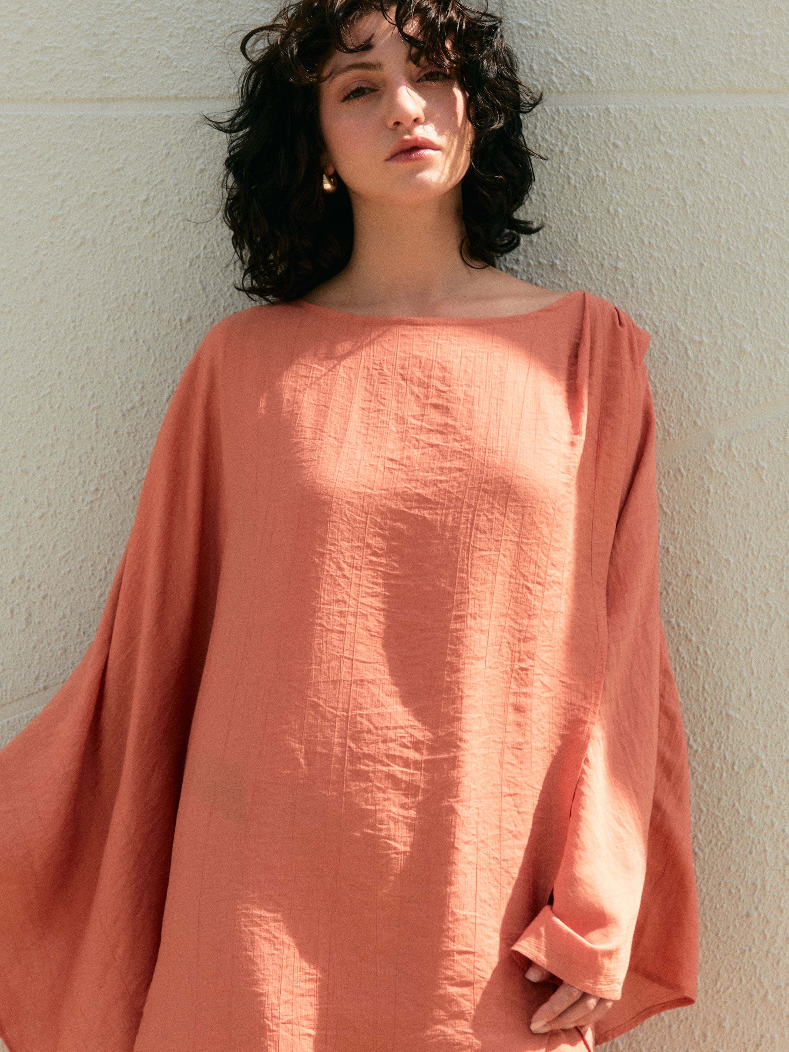 Woman wearing a peach-colored mini kaftan dress against a light background -Coral swim cover up mini kaftan dress top, flowy oversized tunic for beach and pool, airy drape with long sleeves and high low hem