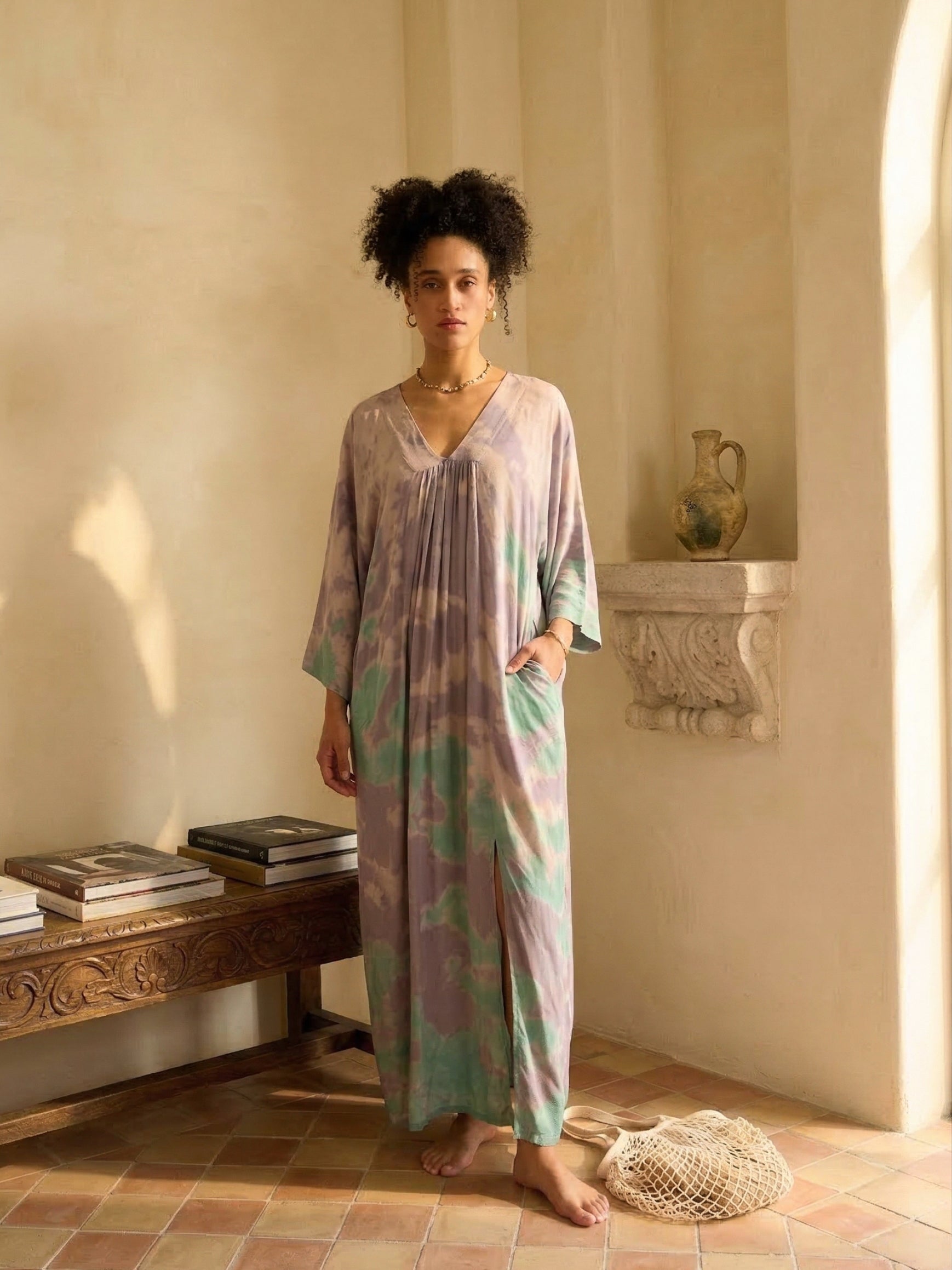 Woman wearing a tie-dye kaftan resort dress in a warm, sunlit room.