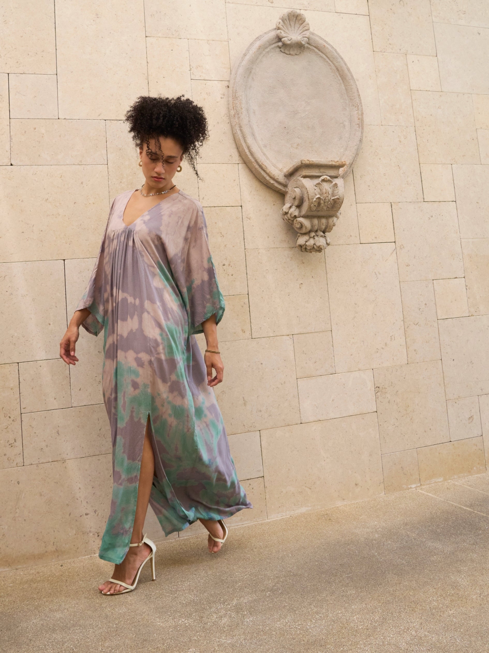 Woman wearing a long, flowing kaftan maxi dress standing against a stone wall.