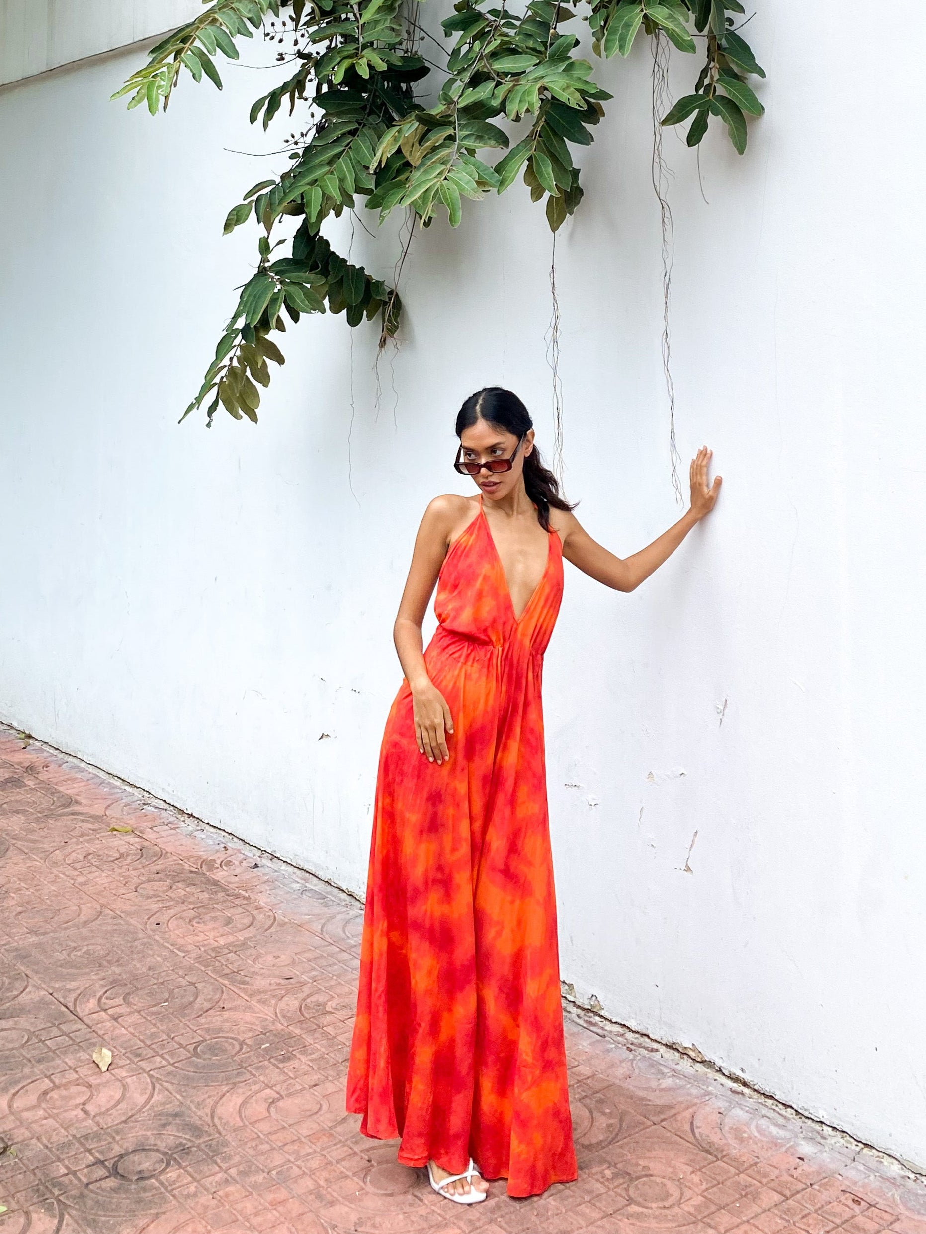 Woman wearing an orange tie-dye open Back Halter Maxi Dress in vibrant orange tie-dye, featuring a flowing maxi length and backless halter design—perfect vacation dress by Coco De Chom.
