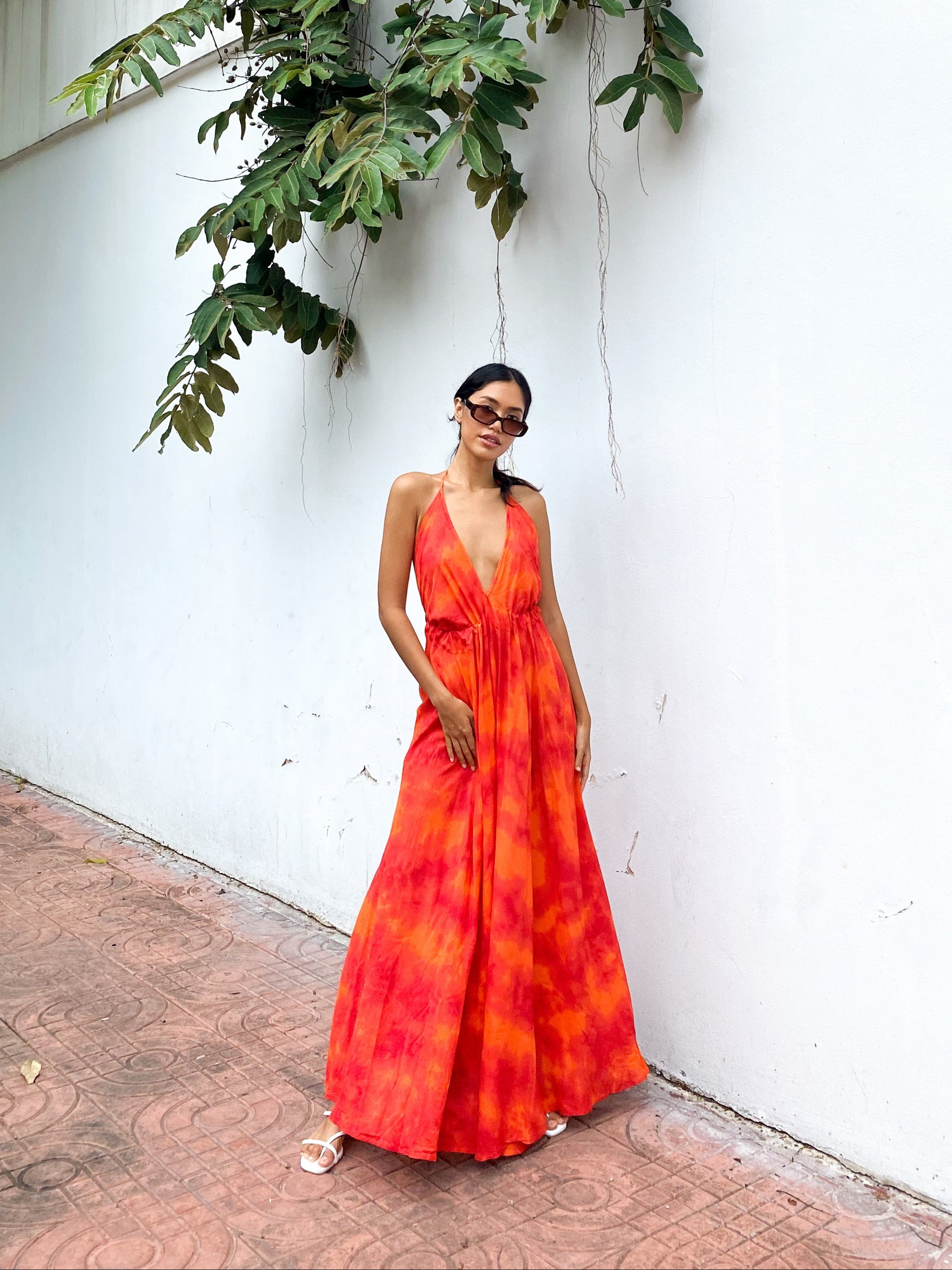 Woman wearing an orange tie-dye open Back Halter Maxi Dress in vibrant orange tie-dye, featuring a flowing maxi length and backless halter design—perfect vacation dress by Coco De Chom.
